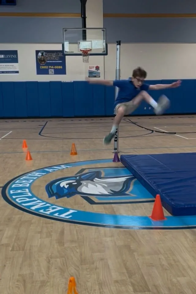 boy jumps over cones in gymnasium