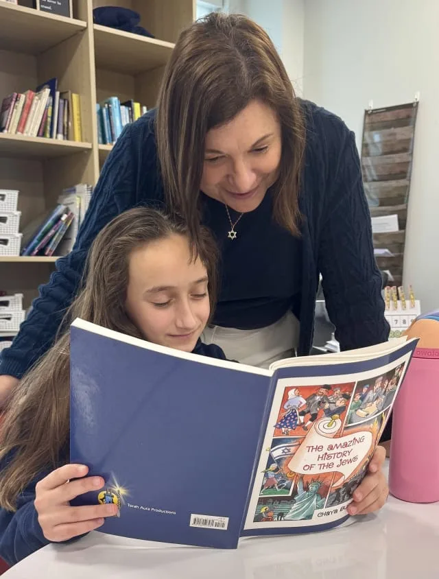 teacher looks over girls shoulder while she reads about the history of the Jews