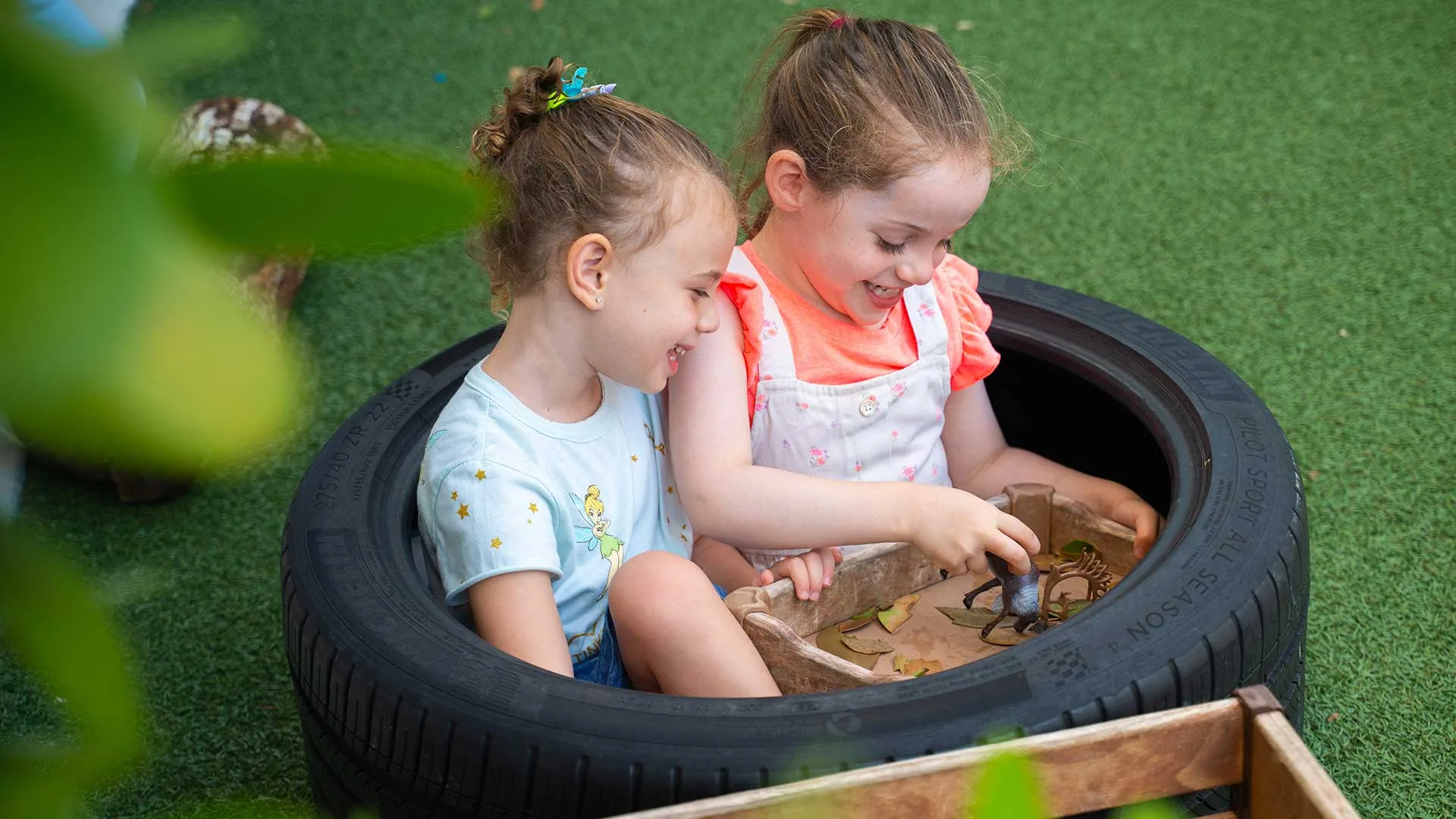 two girls sitting in a tire at the playground