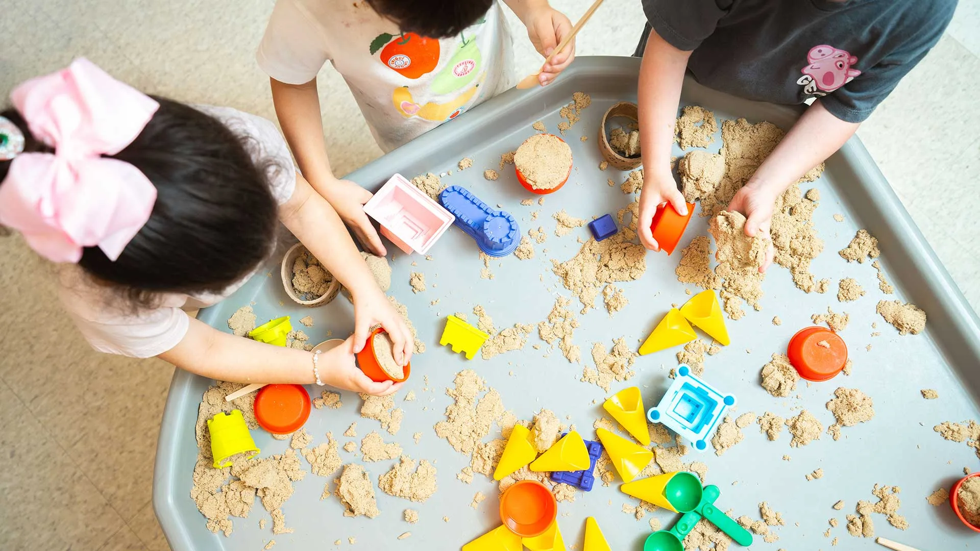 3 children play with toys in a sandbox