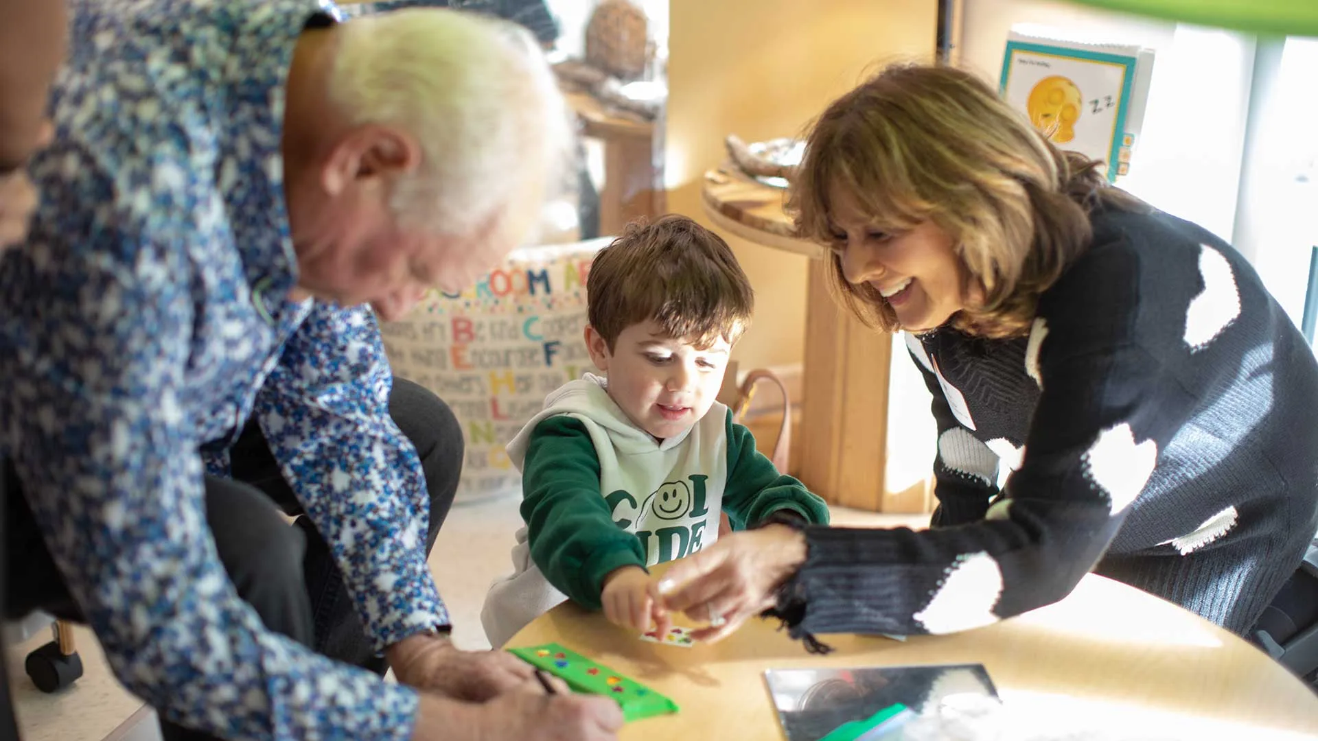 senior man works on a craft project with a boy while the teacher helps